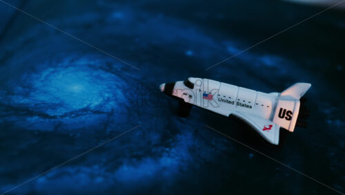 Close up of a miniature toy space shuttle placed on a blue cosmic galaxy backdrop - Starpik Stock