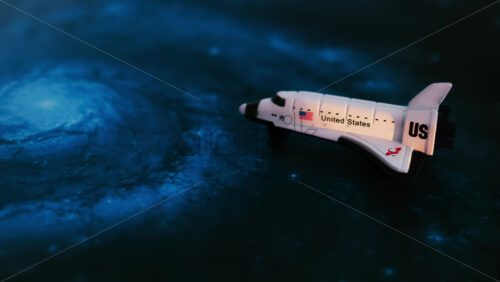 Close up of a miniature toy space shuttle placed on a blue cosmic galaxy backdrop - Starpik Stock