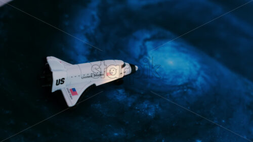 Close up of a miniature toy space shuttle placed on a blue cosmic galaxy backdrop - Starpik Stock