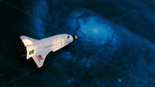 Close up of a miniature toy space shuttle placed on a blue cosmic galaxy backdrop - Starpik Stock