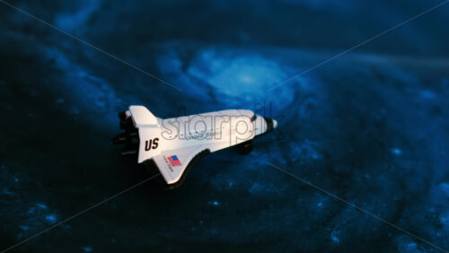 Close up of a miniature toy space shuttle placed on a blue cosmic galaxy backdrop - Starpik Stock