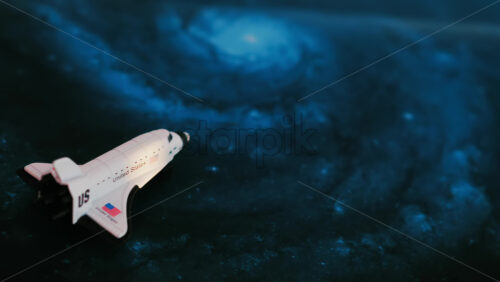 Close up of a miniature toy space shuttle placed on a blue cosmic galaxy backdrop - Starpik Stock