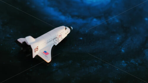 Close up of a miniature toy space shuttle placed on a blue cosmic galaxy backdrop - Starpik Stock