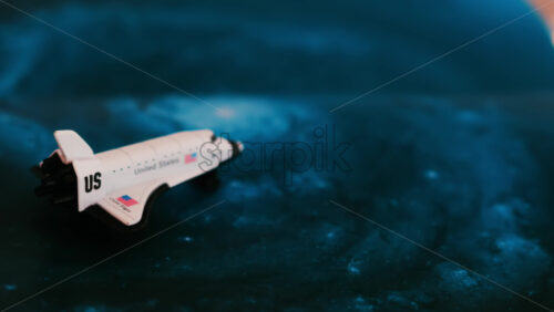 Close up of a miniature toy space shuttle placed on a blue cosmic galaxy backdrop - Starpik Stock
