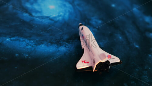 Close up of a miniature toy space shuttle placed on a blue cosmic galaxy backdrop - Starpik Stock