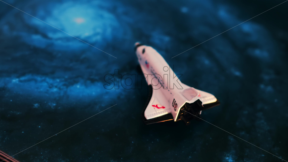 Close up of a miniature toy space shuttle placed on a blue cosmic galaxy backdrop - Starpik Stock