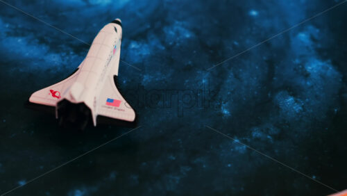 Close up of a miniature toy space shuttle placed on a blue cosmic galaxy backdrop - Starpik Stock
