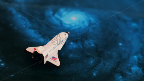 Close up of a miniature toy space shuttle placed on a blue cosmic galaxy backdrop - Starpik Stock