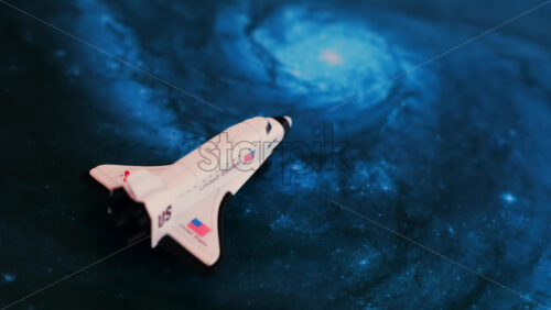 Close up of a miniature toy space shuttle placed on a blue cosmic galaxy backdrop - Starpik Stock