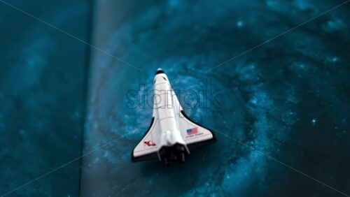 Close up of a miniature toy space shuttle placed on a blue cosmic galaxy backdrop - Starpik Stock