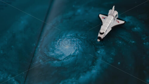 Close up of a miniature toy space shuttle placed on a blue cosmic galaxy backdrop - Starpik Stock