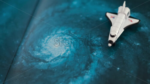 Close up of a miniature toy space shuttle placed on a blue cosmic galaxy backdrop - Starpik Stock