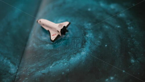Close up of a miniature toy space shuttle placed on a blue cosmic galaxy backdrop - Starpik Stock