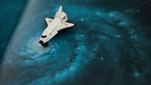Close up of a miniature toy space shuttle placed on a blue cosmic galaxy backdrop - Starpik Stock