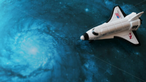 Close up of a miniature toy space shuttle placed on a blue cosmic galaxy backdrop - Starpik Stock