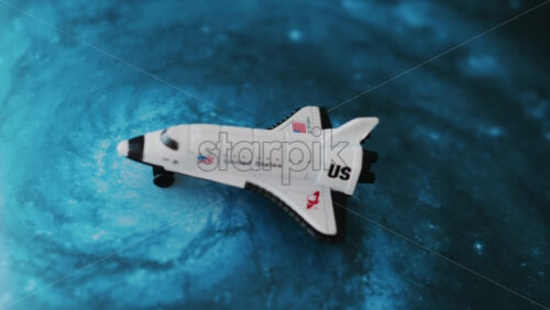 Close up of a miniature toy space shuttle placed on a blue cosmic galaxy backdrop - Starpik Stock