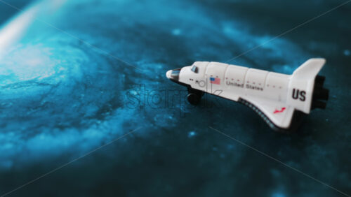 Close up of a miniature toy space shuttle placed on a blue cosmic galaxy backdrop - Starpik Stock