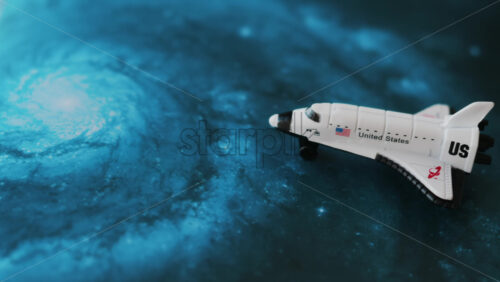 Close up of a miniature toy space shuttle placed on a blue cosmic galaxy backdrop - Starpik Stock