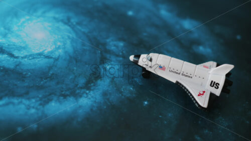 Close up of a miniature toy space shuttle placed on a blue cosmic galaxy backdrop - Starpik Stock