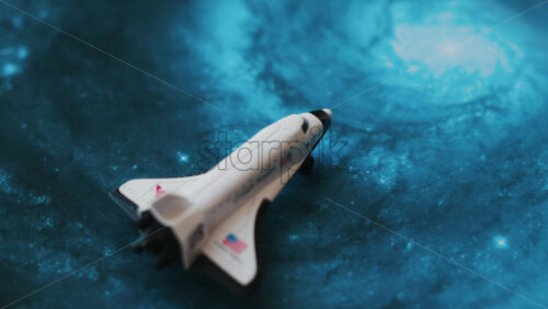 Close up of a miniature toy space shuttle placed on a blue cosmic galaxy backdrop - Starpik Stock