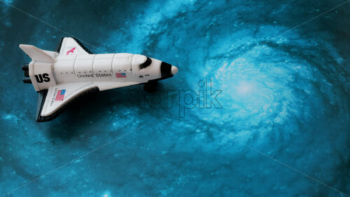 Close up of a miniature toy space shuttle placed on a blue cosmic galaxy backdrop - Starpik Stock