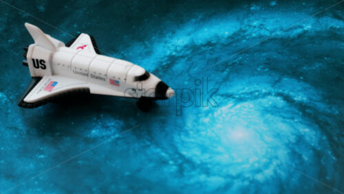 Close up of a miniature toy space shuttle placed on a blue cosmic galaxy backdrop - Starpik Stock