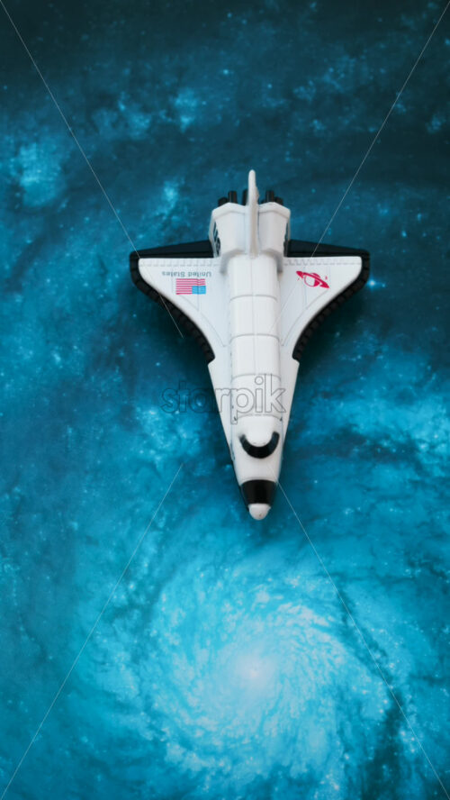 Close up of a miniature toy space shuttle placed on a blue cosmic galaxy backdrop - Starpik Stock