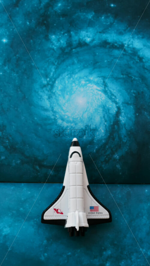 Close up of a miniature toy space shuttle placed on a blue cosmic galaxy backdrop - Starpik Stock