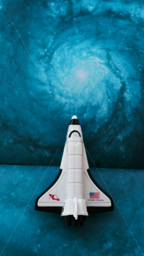 Close up of a miniature toy space shuttle placed on a blue cosmic galaxy backdrop - Starpik Stock