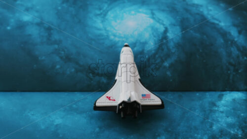 Close up of a miniature toy space shuttle placed on a blue cosmic galaxy backdrop - Starpik Stock