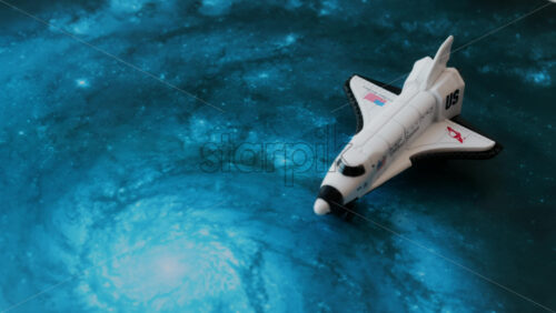 Close up of a miniature toy space shuttle placed on a blue cosmic galaxy backdrop - Starpik Stock