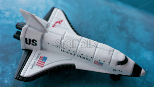 Close up of a miniature toy space shuttle placed on a blue cosmic galaxy backdrop - Starpik Stock