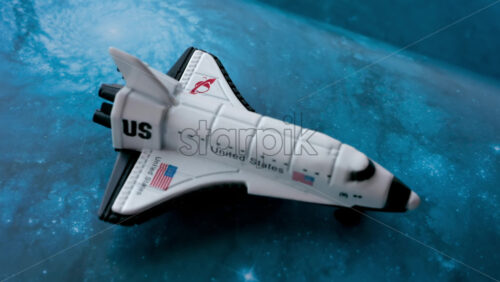Close up of a miniature toy space shuttle placed on a blue cosmic galaxy backdrop - Starpik Stock