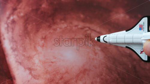 Close up of a miniature toy space shuttle placed on a reddish galaxy background - Starpik Stock