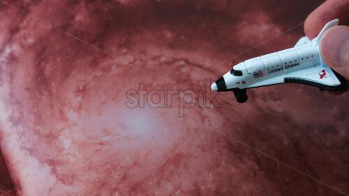 Close up of a miniature toy space shuttle placed on a reddish galaxy background - Starpik Stock