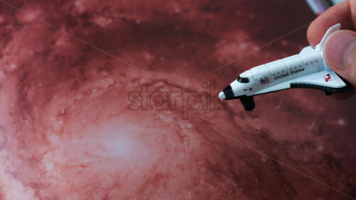 Close up of a miniature toy space shuttle placed on a reddish galaxy background - Starpik Stock