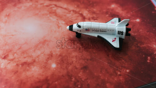 Close up of a miniature toy space shuttle placed on a reddish galaxy background - Starpik Stock