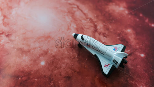 Close up of a miniature toy space shuttle placed on a reddish galaxy background - Starpik Stock