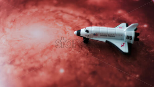 Close up of a miniature toy space shuttle placed on a reddish galaxy background - Starpik Stock