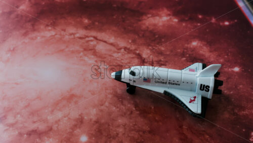 Close up of a miniature toy space shuttle placed on a reddish galaxy background - Starpik Stock