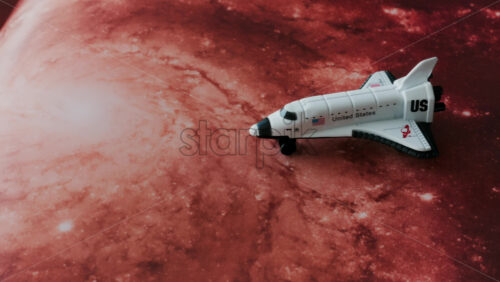 Close up of a miniature toy space shuttle placed on a reddish galaxy background - Starpik Stock