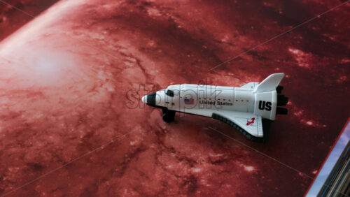 Close up of a miniature toy space shuttle placed on a reddish galaxy background - Starpik Stock