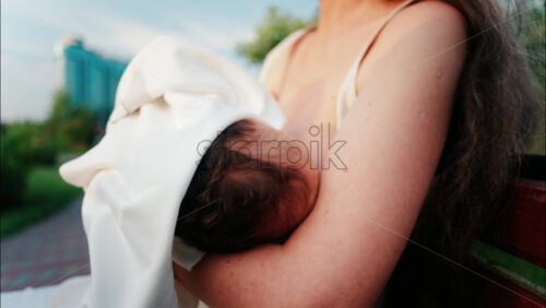 Close up of a mother holding her newborn in her arms outdoors during sunset - Starpik Stock