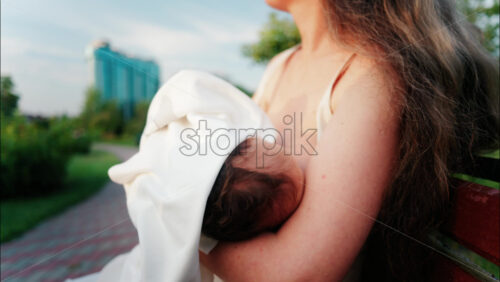Close up of a mother holding her newborn in her arms outdoors during sunset - Starpik Stock