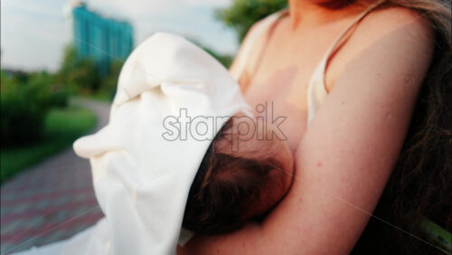 Close up of a mother holding her newborn in her arms outdoors during sunset - Starpik Stock