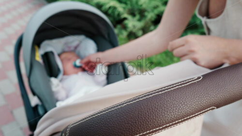 Close up of a mother placing a pacifier into a baby’s mouth while seated in a stroller - Starpik Stock
