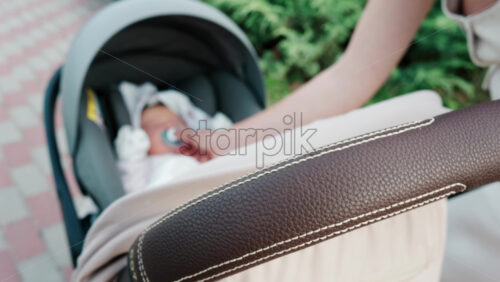 Close up of a mother placing a pacifier into a baby’s mouth while seated in a stroller - Starpik Stock
