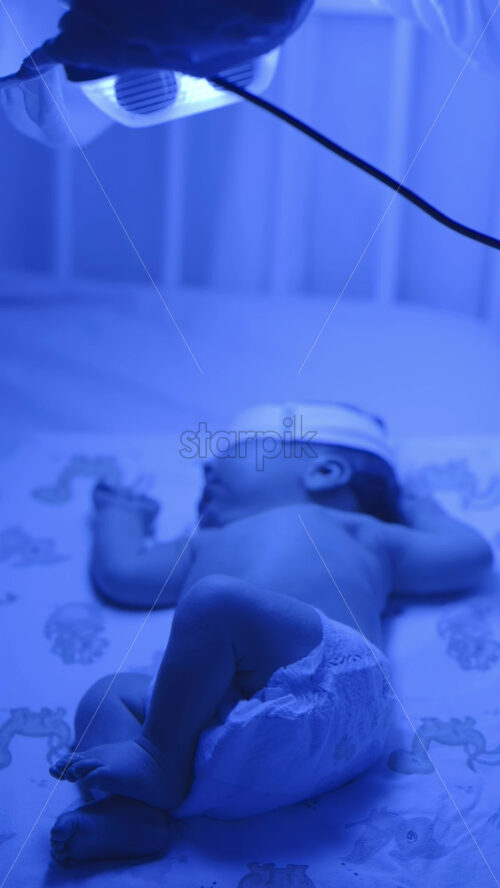 Close up of a newborn baby moving around on a crib mattress, wearing a diaper with calming blue lighting. Vertical - Starpik Stock