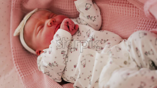 Close up of a newborn baby sleeping on a pink blanket, dressed in patterned pajamas - Starpik Stock
