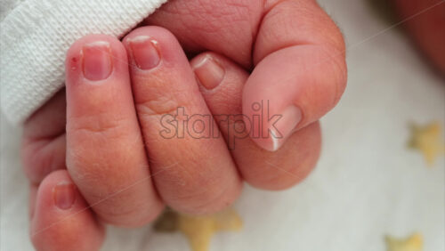 Close up of a newborn baby’s tiny hand clenched in soft natural light while resting - Starpik Stock